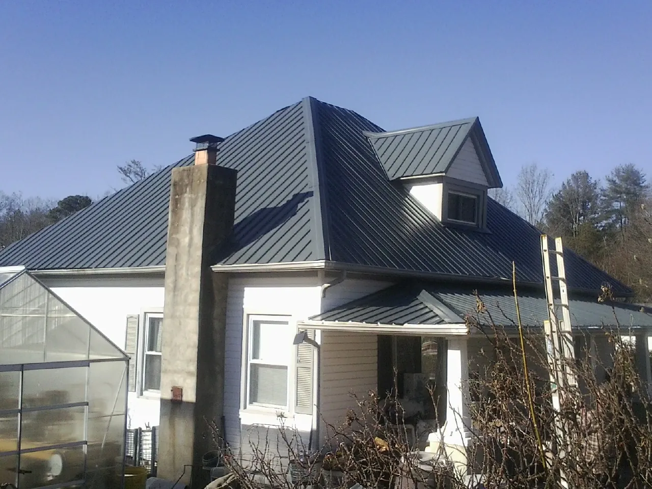 Dark blue standing seam metal roof on a white farmhouse with dormer — Slate & Tile Roof Repair by Roofing Brothers in Bondsville