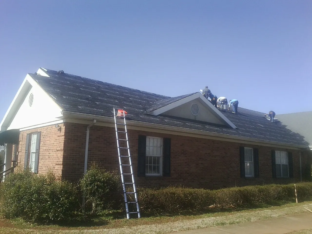Crew tearing shingles off a brick ranch roof with a ladder set — Emergency Roof Repair work by our crew in Bondsville