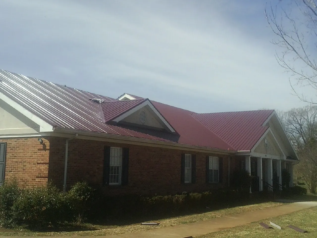 Red metal roof with gabled entries on a long brick building, from a Hail Damage Roof Repair job in Bondsville