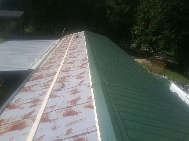 Old rusted panels beside newly installed green metal roofing — Wind Damage Roof Repair by Roofing Brothers in Bondsville