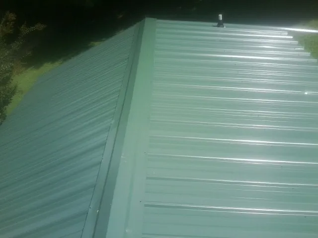 New green metal panels meeting at the ridge of a roof — Flat Roof Repair work by our crew in Bondsville