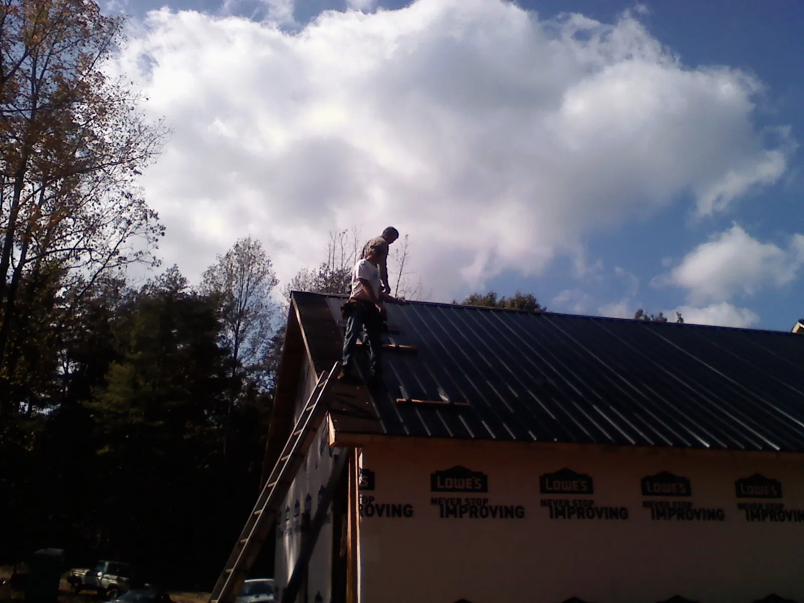 Roofer fastening dark metal panels high against a cloudy sky, from a Roof Inspection job in Bondsville