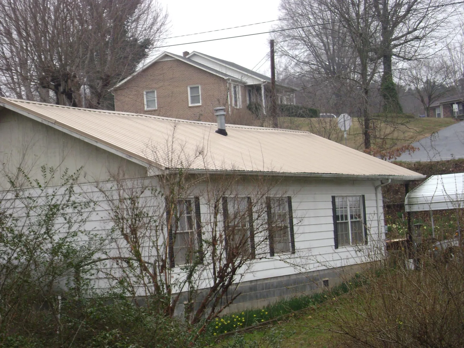 Tan metal roof on a white sided house set into a hillside — Commercial Roofing by Roofing Brothers in Bondsville